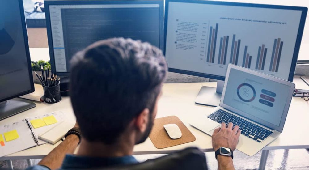 Man creating statistics in modern office. He working on digital devices while sitting at table and turning back to camera